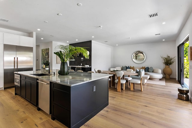 kitchen with built in appliances, light stone counters, sink, and an island with sink