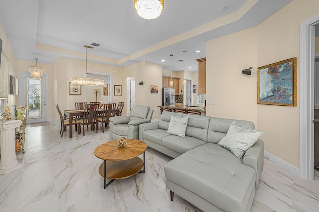 living room with a notable chandelier, sink, and a tray ceiling