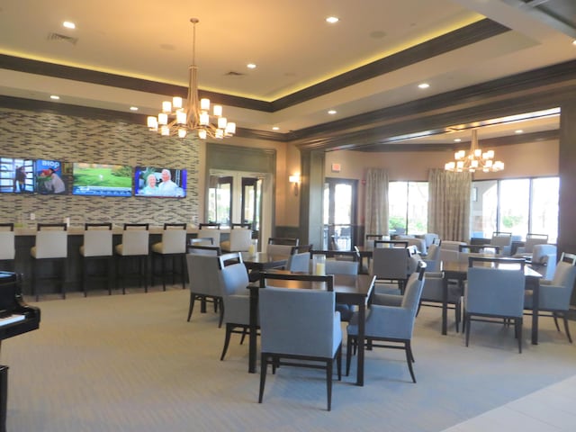 carpeted dining space featuring ornamental molding, a raised ceiling, and a notable chandelier