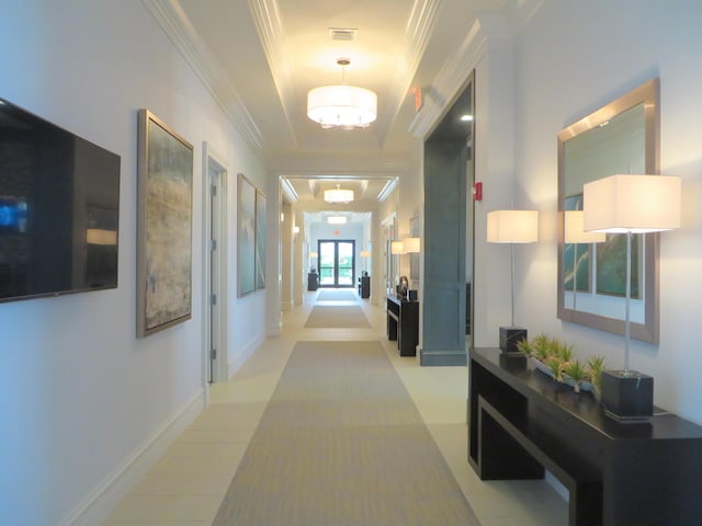 corridor featuring crown molding, light tile patterned floors, an inviting chandelier, and a tray ceiling