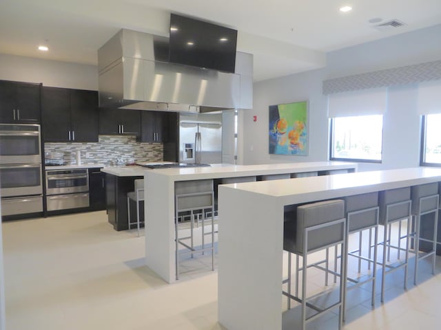 kitchen with appliances with stainless steel finishes, a center island, a kitchen bar, tasteful backsplash, and island range hood