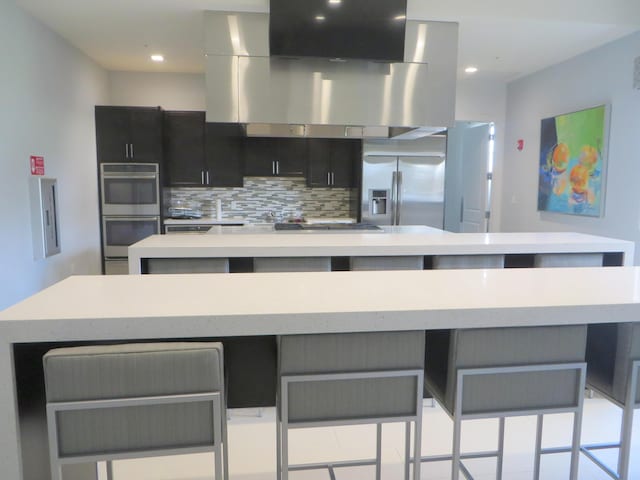 kitchen featuring island range hood, a breakfast bar area, appliances with stainless steel finishes, decorative backsplash, and a spacious island