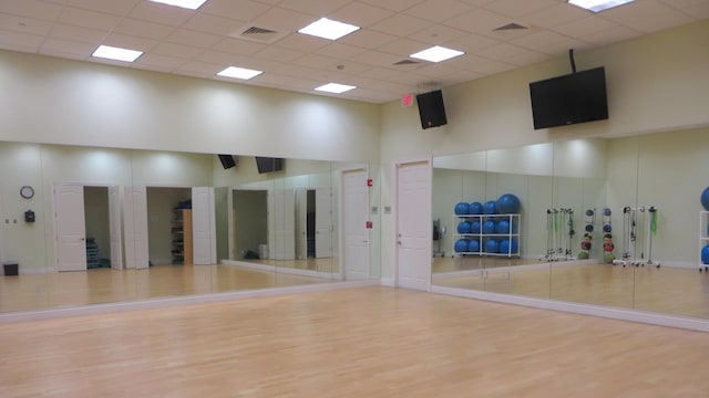 workout room with a paneled ceiling, light wood-type flooring, and a high ceiling