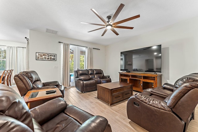 living room with a textured ceiling, light hardwood / wood-style flooring, and ceiling fan