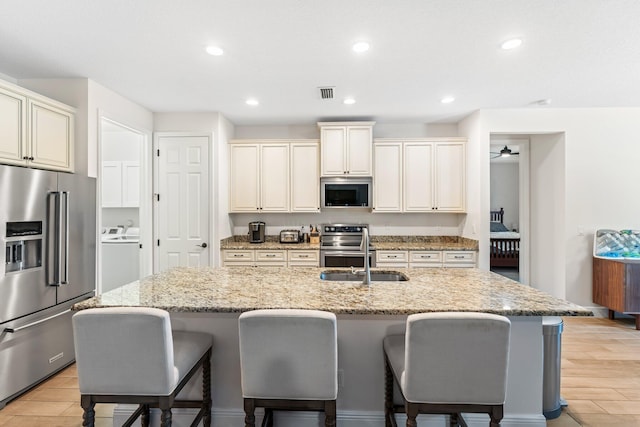 kitchen with stainless steel appliances, light stone counters, a center island with sink, and sink