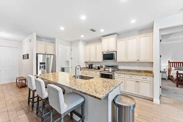 kitchen featuring light stone countertops, stainless steel appliances, a center island with sink, and sink