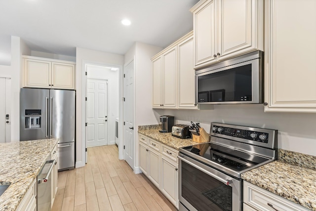 kitchen with light stone countertops, cream cabinetry, stainless steel appliances, and light hardwood / wood-style flooring