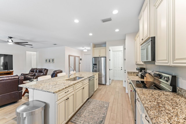 kitchen featuring a center island with sink, sink, ceiling fan, light stone countertops, and appliances with stainless steel finishes