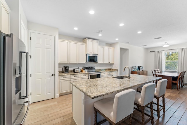 kitchen featuring light stone countertops, appliances with stainless steel finishes, a kitchen breakfast bar, sink, and a center island with sink