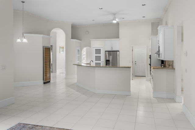 kitchen with a towering ceiling, pendant lighting, stainless steel refrigerator with ice dispenser, white cabinetry, and ceiling fan with notable chandelier