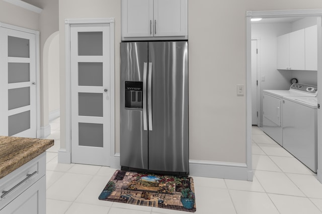 kitchen featuring white cabinets, dark stone countertops, light tile patterned floors, stainless steel fridge with ice dispenser, and washing machine and dryer