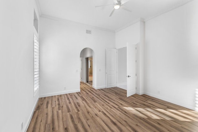 empty room featuring a high ceiling, hardwood / wood-style flooring, ceiling fan, and crown molding