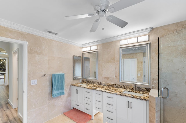 bathroom with tile walls, ornamental molding, ceiling fan, a shower with door, and vanity