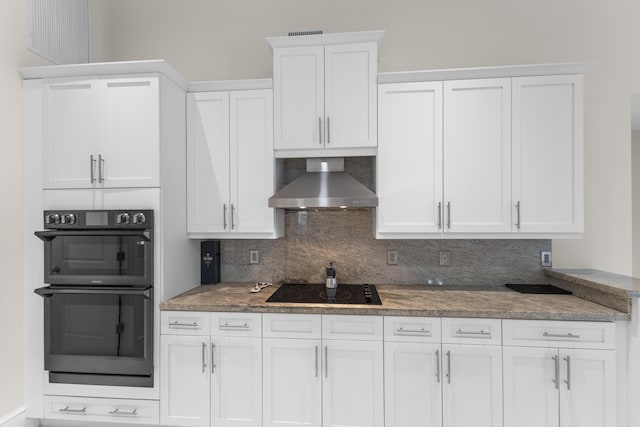 kitchen with black appliances, white cabinetry, wall chimney range hood, and decorative backsplash