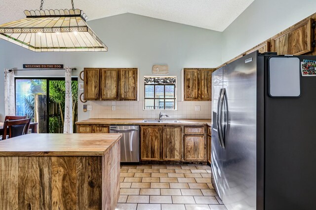 kitchen featuring lofted ceiling, backsplash, sink, light tile patterned flooring, and stainless steel appliances