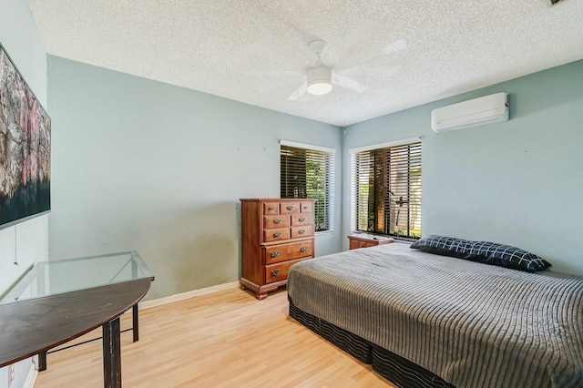 bedroom featuring ceiling fan, light wood-type flooring, a textured ceiling, and a wall mounted AC