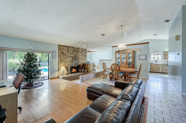 living room with rail lighting, vaulted ceiling, wood-type flooring, a notable chandelier, and a stone fireplace