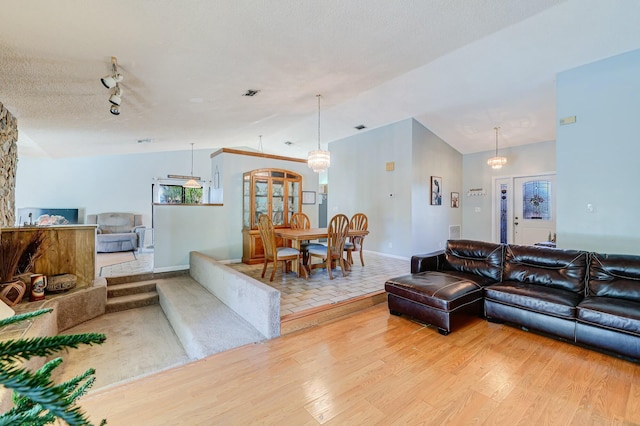 living room featuring rail lighting, hardwood / wood-style floors, a chandelier, a textured ceiling, and vaulted ceiling