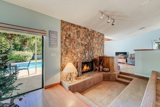 living room featuring a fireplace, a textured ceiling, light hardwood / wood-style floors, and track lighting