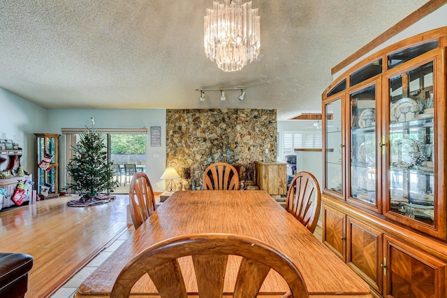 dining space with a textured ceiling, light wood-type flooring, track lighting, and an inviting chandelier