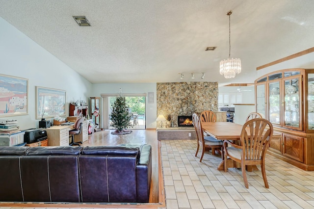 living room with rail lighting, a textured ceiling, a notable chandelier, a stone fireplace, and lofted ceiling