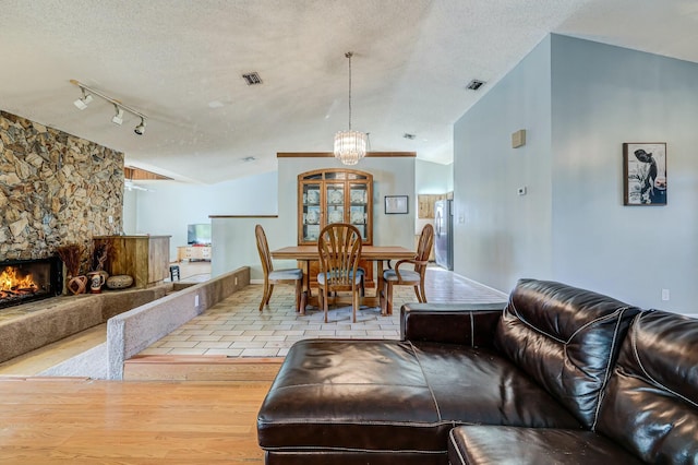 living room with a fireplace, vaulted ceiling, track lighting, and light hardwood / wood-style flooring