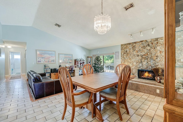 dining room featuring track lighting, an inviting chandelier, vaulted ceiling, a textured ceiling, and a fireplace