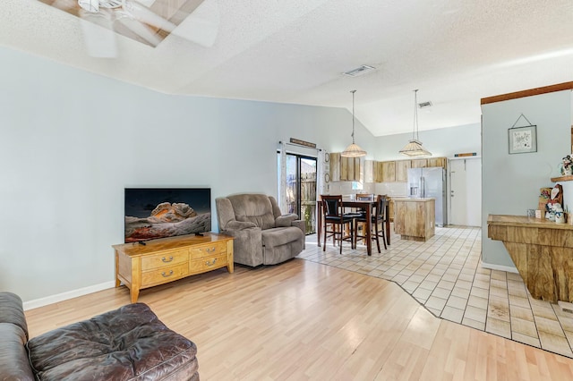 living room with vaulted ceiling, ceiling fan, light hardwood / wood-style floors, and a textured ceiling