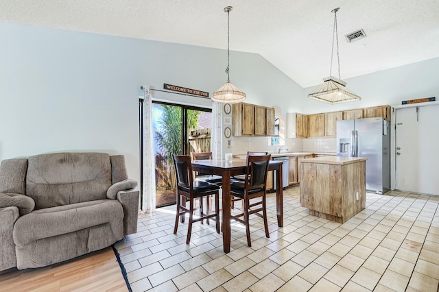 dining room with a textured ceiling, light hardwood / wood-style flooring, vaulted ceiling, and sink