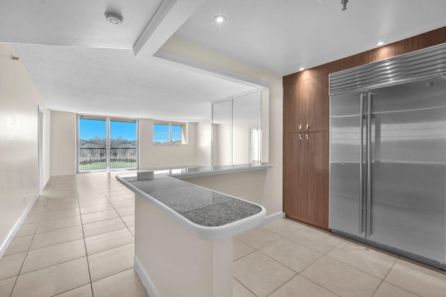 kitchen featuring built in refrigerator, kitchen peninsula, floor to ceiling windows, and light tile patterned floors