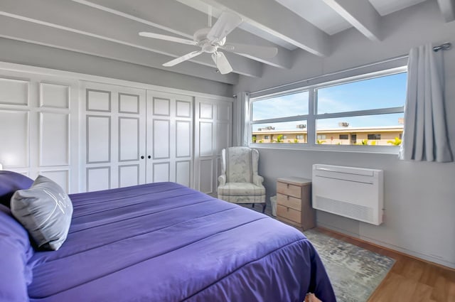 bedroom featuring heating unit, ceiling fan, beamed ceiling, and wood-type flooring