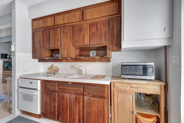 kitchen with oven, sink, decorative backsplash, light tile patterned floors, and tile counters