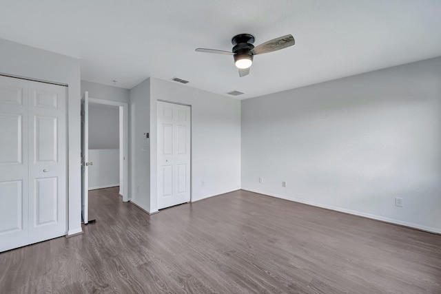 unfurnished bedroom featuring ceiling fan, dark hardwood / wood-style flooring, and two closets