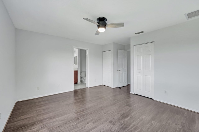 unfurnished bedroom featuring ceiling fan, dark hardwood / wood-style floors, multiple closets, and ensuite bath