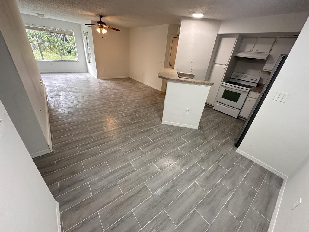 kitchen with gray cabinetry, white electric stove, a textured ceiling, kitchen peninsula, and stainless steel refrigerator