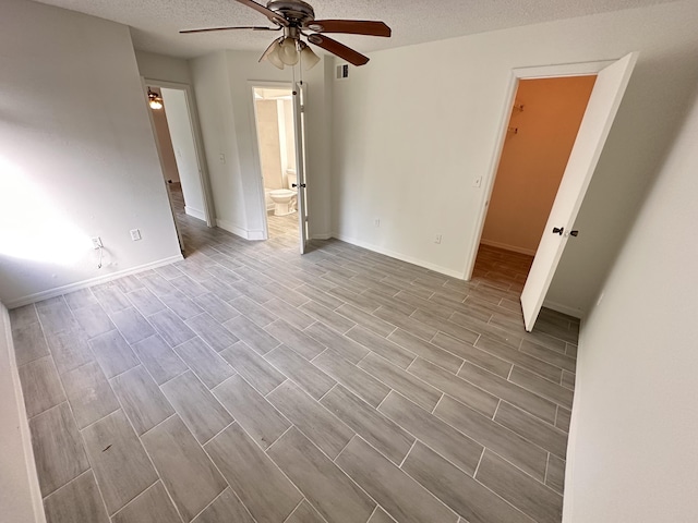 unfurnished bedroom featuring visible vents, baseboards, ensuite bath, a textured ceiling, and wood finish floors