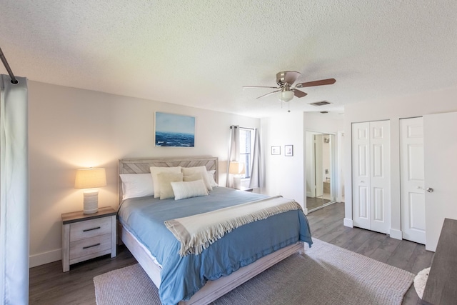 bedroom featuring a textured ceiling, ceiling fan, dark wood-type flooring, and multiple closets