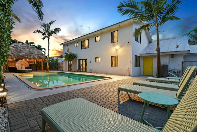 pool at dusk with a gazebo, a patio area, and central air condition unit