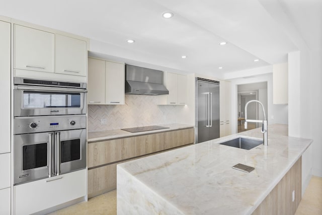 kitchen with sink, light stone countertops, stainless steel appliances, wall chimney exhaust hood, and cream cabinets