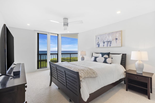 bedroom featuring ceiling fan, light colored carpet, access to outside, a water view, and a wall of windows