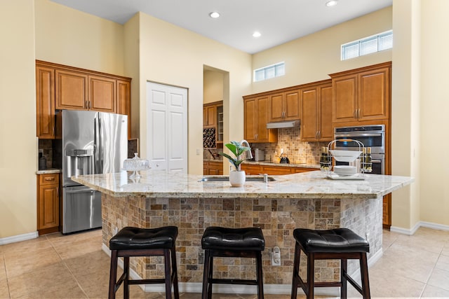 kitchen featuring appliances with stainless steel finishes, backsplash, a large island with sink, light stone counters, and a breakfast bar