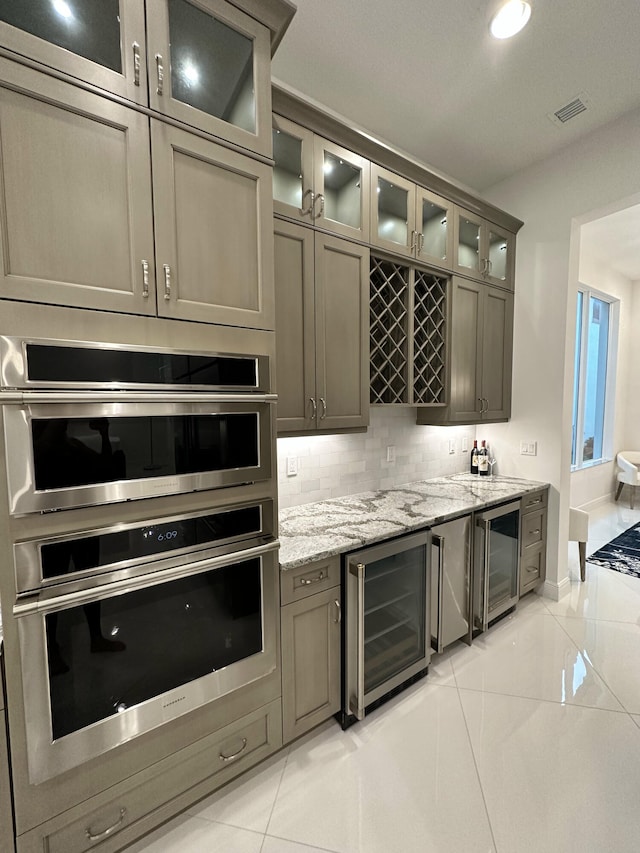 kitchen with wine cooler, light stone countertops, light tile patterned floors, and stainless steel double oven