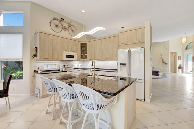 kitchen with a kitchen bar, white appliances, dark stone countertops, an island with sink, and light tile patterned flooring