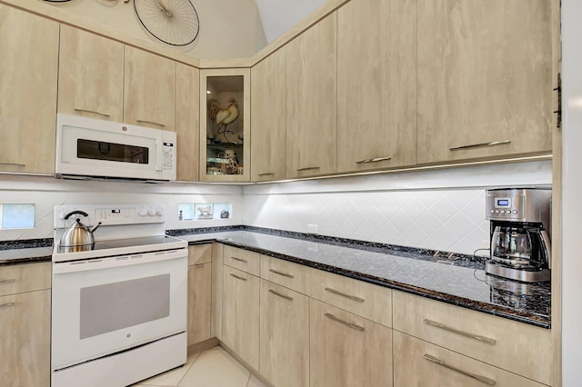 kitchen featuring light brown cabinetry, light tile patterned floors, dark stone counters, and white appliances