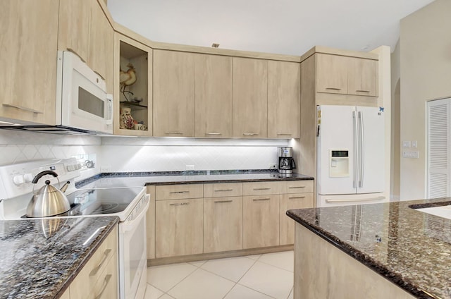 kitchen with backsplash, dark stone counters, white appliances, light brown cabinets, and light tile patterned floors