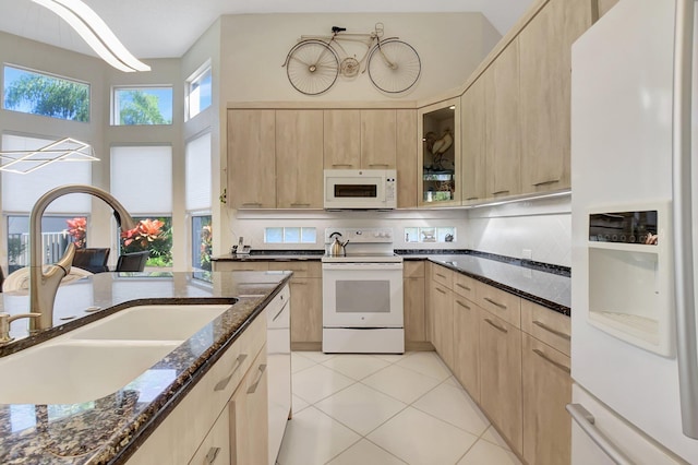 kitchen featuring white appliances, dark stone counters, sink, light tile patterned floors, and light brown cabinetry