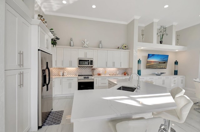 kitchen with a kitchen bar, decorative backsplash, stainless steel appliances, sink, and white cabinetry