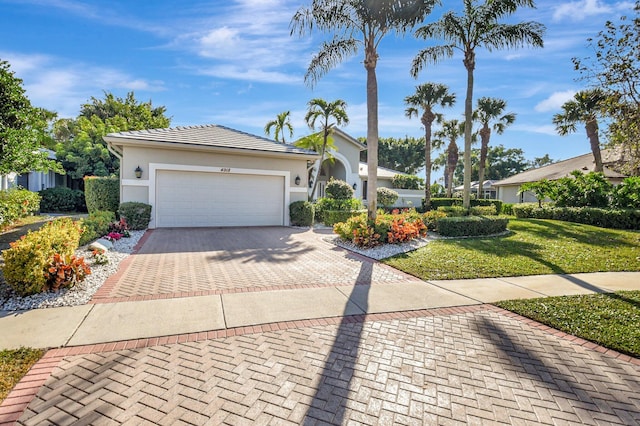 ranch-style home with decorative driveway, stucco siding, an attached garage, a front yard, and a tiled roof