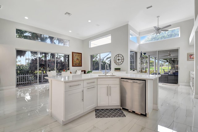 kitchen featuring a center island with sink, sink, stainless steel dishwasher, a towering ceiling, and white cabinetry