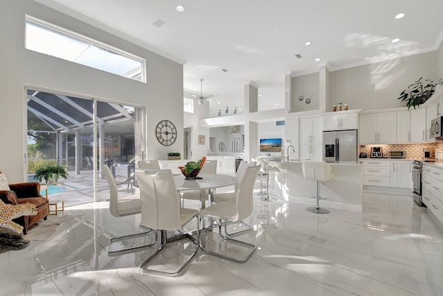 dining space featuring ceiling fan, sink, a towering ceiling, and ornamental molding